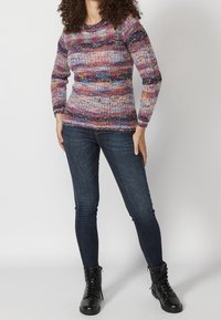 Pull en maille multicolore avec une texture côtelée, un col rond et des manches longues, associé à un jean noir et des bottines noires.