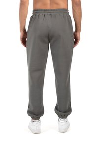 Harmaat collegehousut, joissa on joustava vyötärö ja hihnat, yhdistettynä sileään pintaan. Yhdistetty valkoisiin lenkkikenkiin.