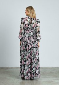 Maxi-jurk met een zwarte achtergrond, voorzien van bloemenpatronen in roze en wit. Gemaakt van doorschijnende stof, met geplooide details en lange mouwen.