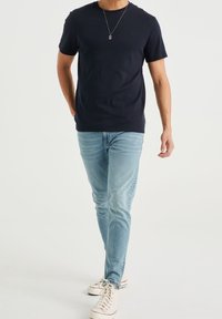 Námořnické bavlněné tričko s krátkými rukávy, kombinované se světle modrými džínami a bílými teniskami. Jednoduchý design bez viditelných vzorů či akcentů.