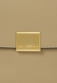 Borsa in pelle beige con hardware rettangolare dorato che presenta il nome del marchio inciso, accentuata da cuciture bianche lungo i bordi.