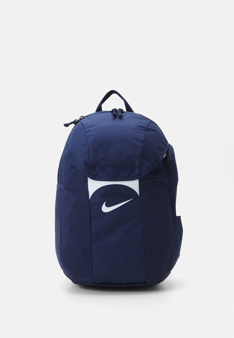 Sac à dos bleu marine au design arrondi, fabriqué en tissu résistant. Il présente un logo Nike blanc bien visible, des straps ajustables et une fermeture éclair.