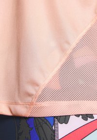 Roze sporttop met een gladde stof en een meshpaneel, met geometrische patronen en contrasterende texturen langs de zoom.