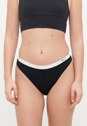 Black bikini bottom featuring a white waistband, three black buttons at the front, and a textured fabric. Full-coverage design.