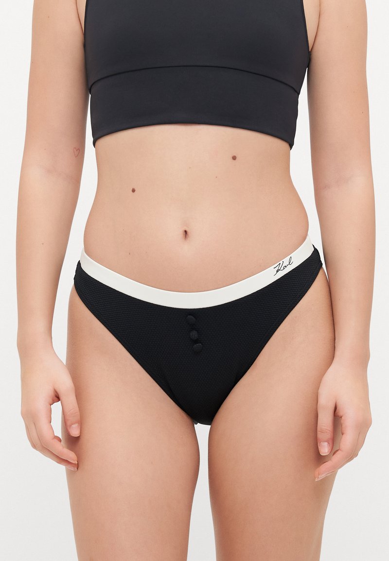 Black bikini bottom featuring a white waistband, three black buttons at the front, and a textured fabric. Full-coverage design.