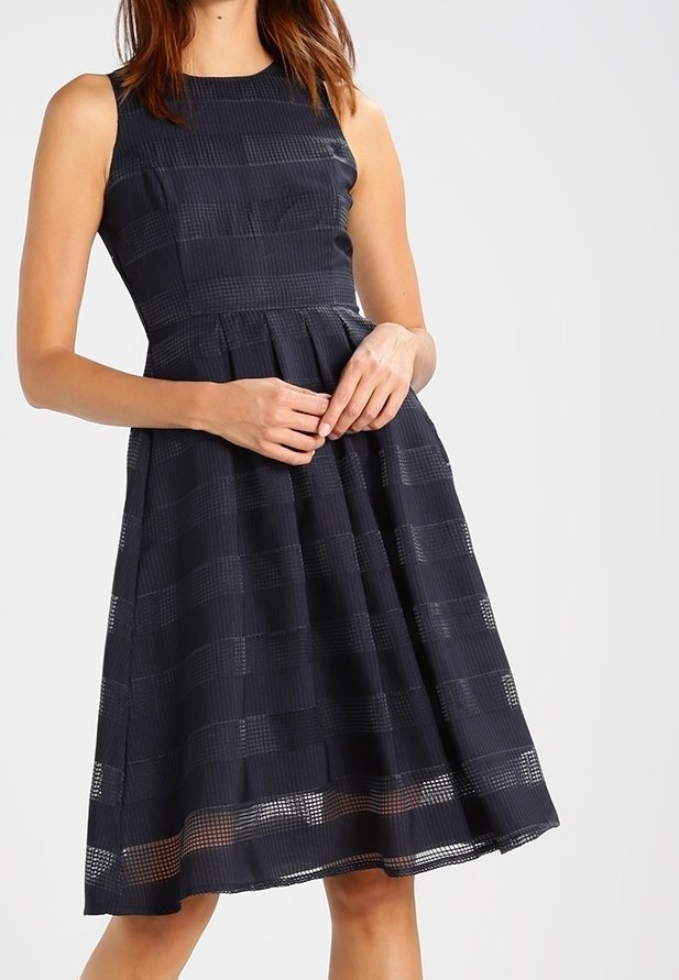 Marinblå ärmlös klänning med ett strukturerat randmönster, figursydd bodice och utsvängd kjol, med längd nedanför knäna och en subtil lyster.