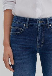 Donkerblauwe denimjeans met een gemiddelde taillehoogte, voorzien van hetelanszakken, contrasterende stiksels en metalen sluitingen.