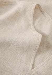Tessuto di lino beige con una texture morbida. Contiene sfumature sottili e una finitura liscia, che mette in evidenza cuciture pulite e bordi arrotondati.
