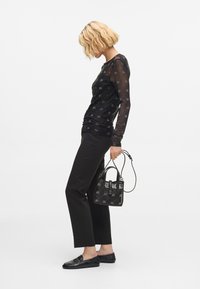 Czarna bluzka z długim rękawem, wykonaną z przezroczystej siateczki z wzorem, połączona z czarnymi spodniami o dopasowanym kroju i loaferami. Całość dopełnia mała czarna torebka.