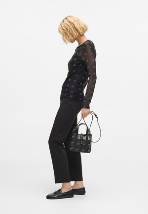 Czarna bluzka z długim rękawem, wykonaną z przezroczystej siateczki z wzorem, połączona z czarnymi spodniami o dopasowanym kroju i loaferami. Całość dopełnia mała czarna torebka.