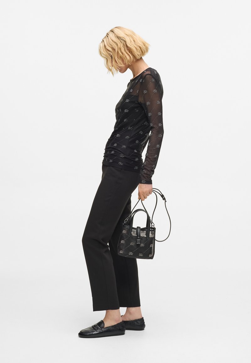 Czarna bluzka z długim rękawem, wykonaną z przezroczystej siateczki z wzorem, połączona z czarnymi spodniami o dopasowanym kroju i loaferami. Całość dopełnia mała czarna torebka.