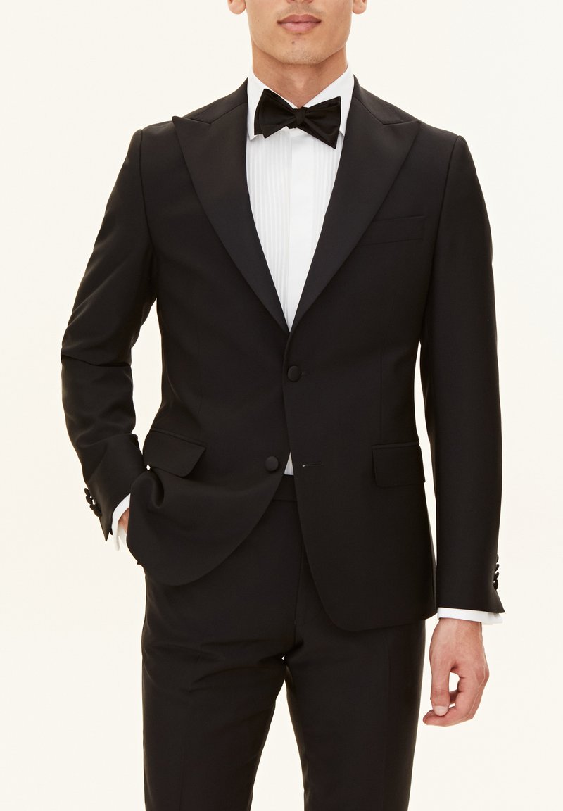 Svart tuxedo med satin krage, enkel knappstängning och vit, plisserad skjorta. Fluga fulländar den formella looken.