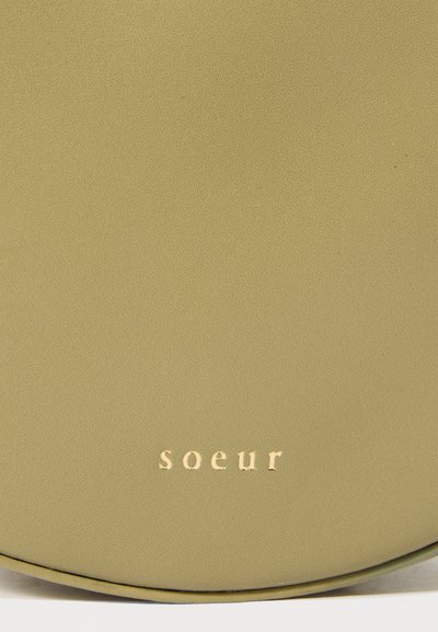 Borsa in pelle verde oliva testurizzata di forma rotonda, con lettering dorato in rilievo che legge "soeur." Design minimalista con bordi lisci.