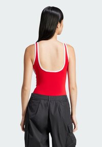 Röd bodysuit med vit trim, med låg rygg och smala band. I kombination med svarta cargo-byxor, som visar en slät tygtextur.