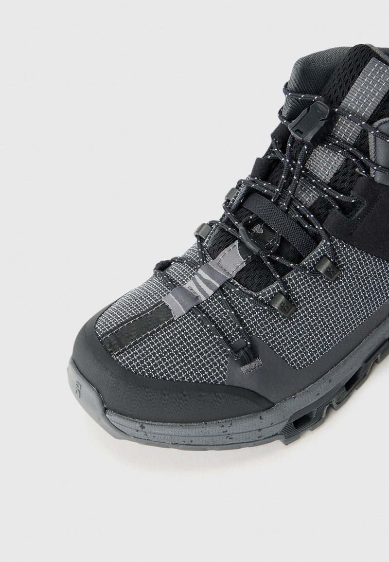 Schwarzer und grauer Wanderstiefel mit einem strukturierten Mesh-Obermaterial, Gummisohle und verstellbarem Schnürsystem, ausgestattet mit einer verstärkten Zehenkappe und detaillierter Nahtführung.