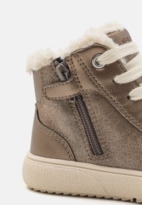 Botas de cuero marrón con forro de lana, costuras de contraste, cremallera lateral y suela de goma texturizada. Cuenta con cordones crema y un acabado brillante.