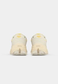 Light beige athletic shoes with a textured upper, yellow accents, and a flexible outsole featuring a Vibram logo.