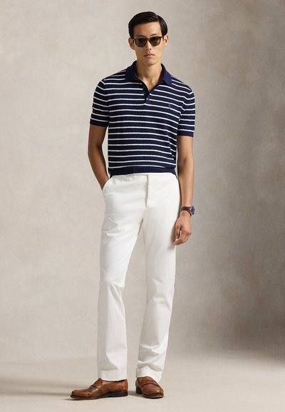 Tengerészkék-fehér csíkos rövid ujjú póló, fehér nadrággal és barna mokaszinokkal párosítva. Kiegészítők: napszemüveg és óra.