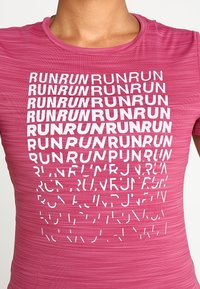 Kortärmad rosa träningsskjorta med ett strukturerat mönster och upprepad text "RUN" i olika storlekar och orienteringar i vitt.