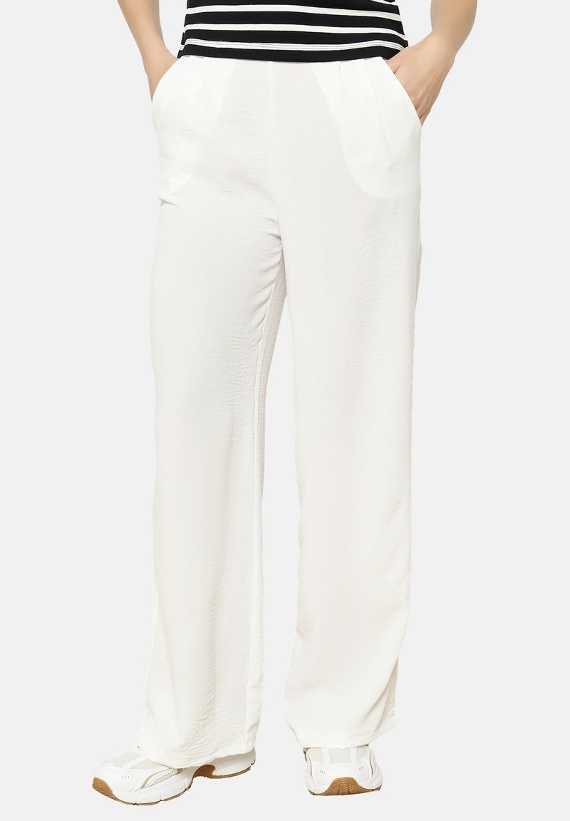 Weiße, weit geschnittene Hosen aus leichtem Stoff, mit schrägen Seitentaschen und einer glatten Textur. Kombiniert mit weißen Sportschuhen.
