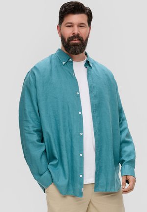 Teal linnen shirt met een knoopsluiting, relaxte pasvorm en lange mouwen over een wit t-shirt. Zachte textuur en minimale hardware-details.