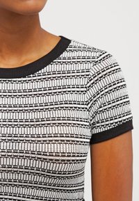 Pletený top s krátkým rukávem v černobílém pruhovaném vzoru, s ribkovaným kulatým výstřihem a texturovanou látkou.