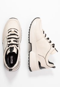 Sneaker beige con un mix di pelle liscia e tessuto strutturato, lacci neri e una suola nera spessa con forma arrotondata.