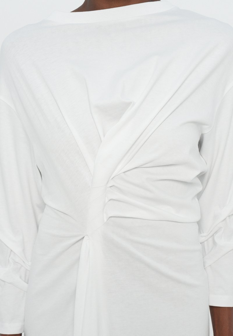 Witte top met lange mouwen, kenmerkend door een gedraaide rugontwerp met geplooide stofdetails, een gladde textuur en een relaxte pasvorm.