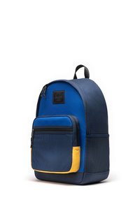 Zaino in tessuto blu con forma arrotondata, tasca frontale in rete, dettagli gialli, manico superiore e patch del logo del brand sulla parte superiore. Chiusure con zip.