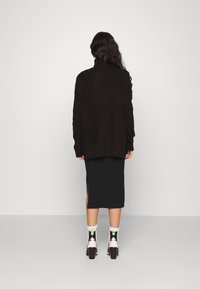 Svart oversized stickad tröja med hög krage, kombinerad med en svart midiklänning med sidslitsar, och mönstrade stövlar i vadlängd.