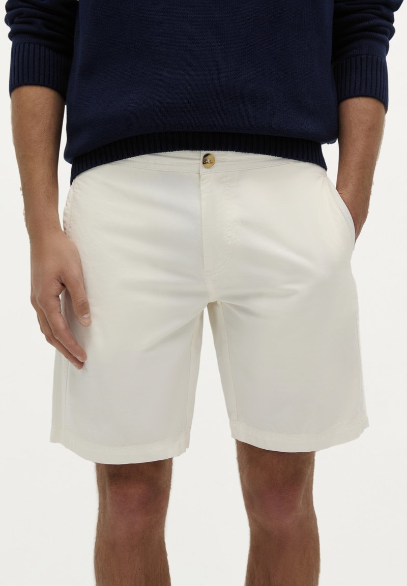 Hvide shorts lavet af et glat stof, med knaplukning og sidelommer. Kanten er ren og lige, og pasformen er afslappet.