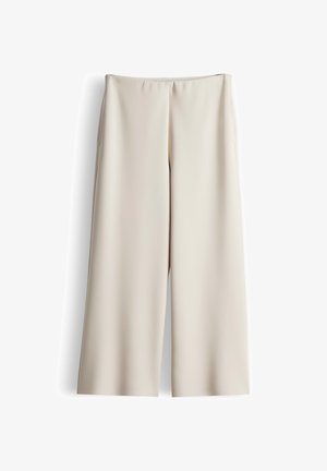 Weit geschnittene Hosen aus glattem, hellbeigem Stoff mit einem elastischen Bund. Sie zeichnen sich durch schlichte, klare Linien aus und haben keine sichtbaren Taschen.