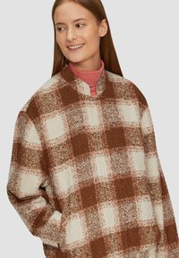 Geruite oversized trui in bruin en crème, met een zachte textuur, hoge halslijn en een kenmerkend ruitpatroon.