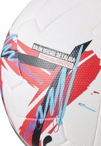 Balts futbola bumbas ar sarkaniem, melnajiem un ziliem grafiskajiem dizainiem. Tam ir teksturēta virsma un uzraksts "BALÓN OFICIAL DE LALIGA Sezona 2024/2025."