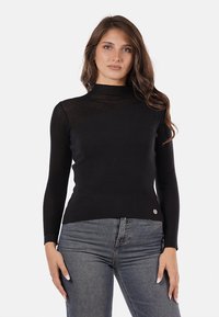 Maglione nero a coste con un collo alto, maniche lunghe e una vestibilità sagomata. Presenta un piccolo logo metallico sul punto vita.