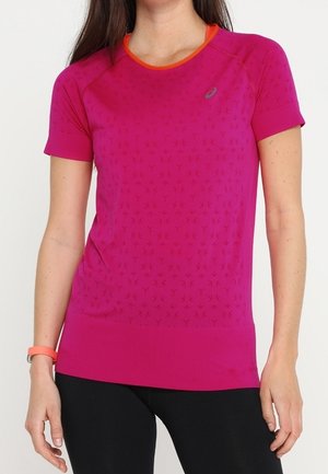 Woman wearing a fitted short-sleeve pink athletic shirt with subtle pattern, orange neckline trim, and black pants against a plain background.