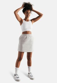Top corto bianco a costine, gonna in jersey grigia con vita elastica, abbinata a scarpe da ginnastica bianche e calze fino al ginocchio.