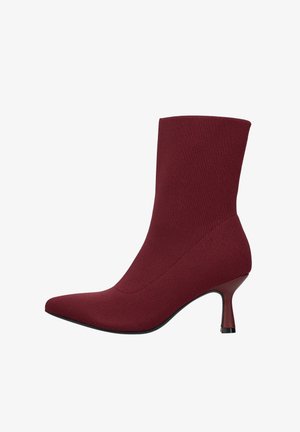 Bordeauxrode enkellaars gemaakt van rekbare stof met een spitse neus en een bescheiden stilettohak. Gladde textuur en naadloos ontwerp.