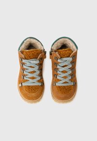 Botine din suede maro cu o căptușeală pufoasă din blană, șireturi albastre și albe și ochiuri metalice. Vârful rotunjit și talpa texturată.