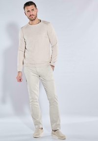 Beige Strickpullover mit gerippten Bündchen, kombiniert mit hellbeigen Cordhosen. Die Schuhe haben ein Passform-Design in einem passenden Farbton.