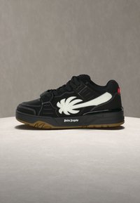 Μαύρο sneaker χαμηλής κορυφής με λευκό σχέδιο φοινικόφυλλου, μαύρα κορδόνια, σόλα από καουτσούκ και λογότυπο "Palm Angels" στο πλάι της σόλας.