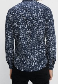 Camicia blu navy con motivo floreale bianco, maniche lunghe, colletto con bottoni e dettaglio sul retro, realizzata in tessuto leggero.