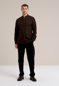 Cămașă button-up de culoare maro închis cu guler mandarin, asortată cu pantaloni negri din catifea și pantofi negri. Design simplu, croială ajustată.
