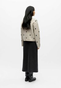 Beige sweater with black polka dots, paired with a long dark skirt and black ankle boots. Smooth texture and relaxed fit. Back view.