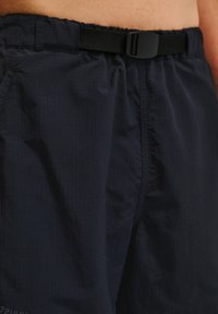 Mörkblå shorts i lätt tyg med ett strukturerat rutmönster, utrustade med ett elastiskt midjeband och ett justerbart svart bälte.