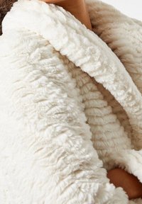 Witte nepbontjas met een weelderige, pluizige textuur en een brede kraag. De stof heeft een geribbeld patroon en een zachte, gezellige uitstraling.