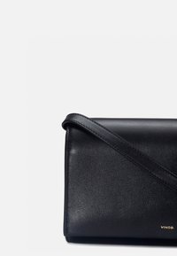 Sac pochette bandoulière en cuir noir avec une sangle fine et un petit logo doré "vince." dans le coin inférieur droit.