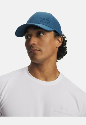 Blue cap with textured fabric, featuring a black Under Armour logo. Worn with a white athletic shirt. Close-up of the model's face.