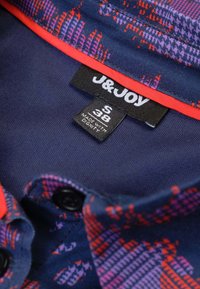 Donkerblauwe shirt met meerkleurige geometrische patronen. Heeft een rode accent rond de kraag, zwarte knopen en een verzorgingslabel binnenin.