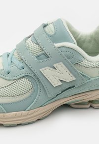 Šviesiai mėlyna sportinė bateliai su tinklo ir sintetiniais paviršiais, su „Velcro“ dirželiu, paminkštintu apvadu ir ryškiu logotipu šone.